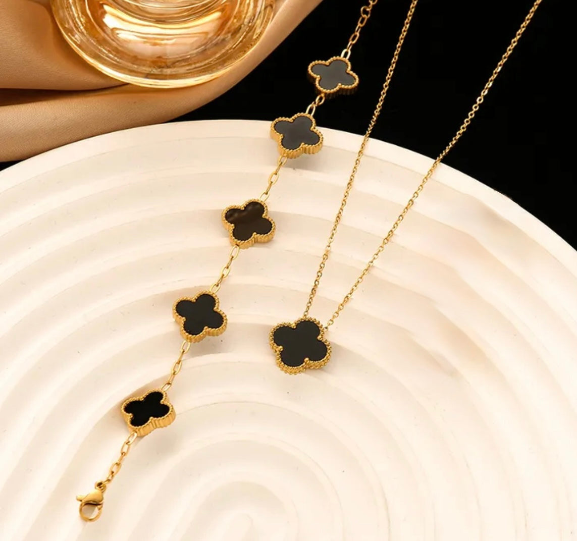 Close up overhead view of elegant 18K gold plated black designer-inspired Van Cleef clover necklace and bracelet set. Lightweight and versatile design, with long lasting, waterproof plating perfect for any occasion, from casual outings to formal events.