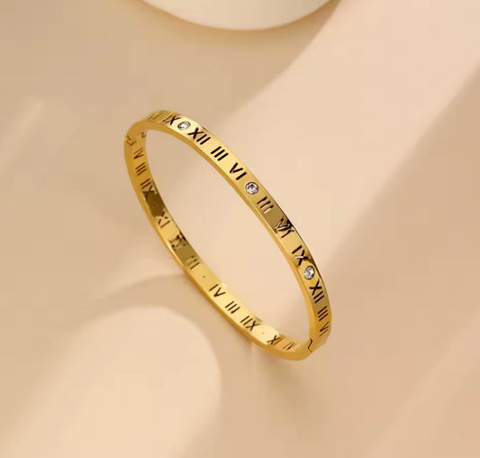 Close up view of elegant 18k Gold plated stainless steel, Cartier dupe, designer inspired, roman numeral bangle bracelet with a smooth, polished finish and inlayed crystals, designed with a lightweight and tarnish resistant material for timeless sophistication.
