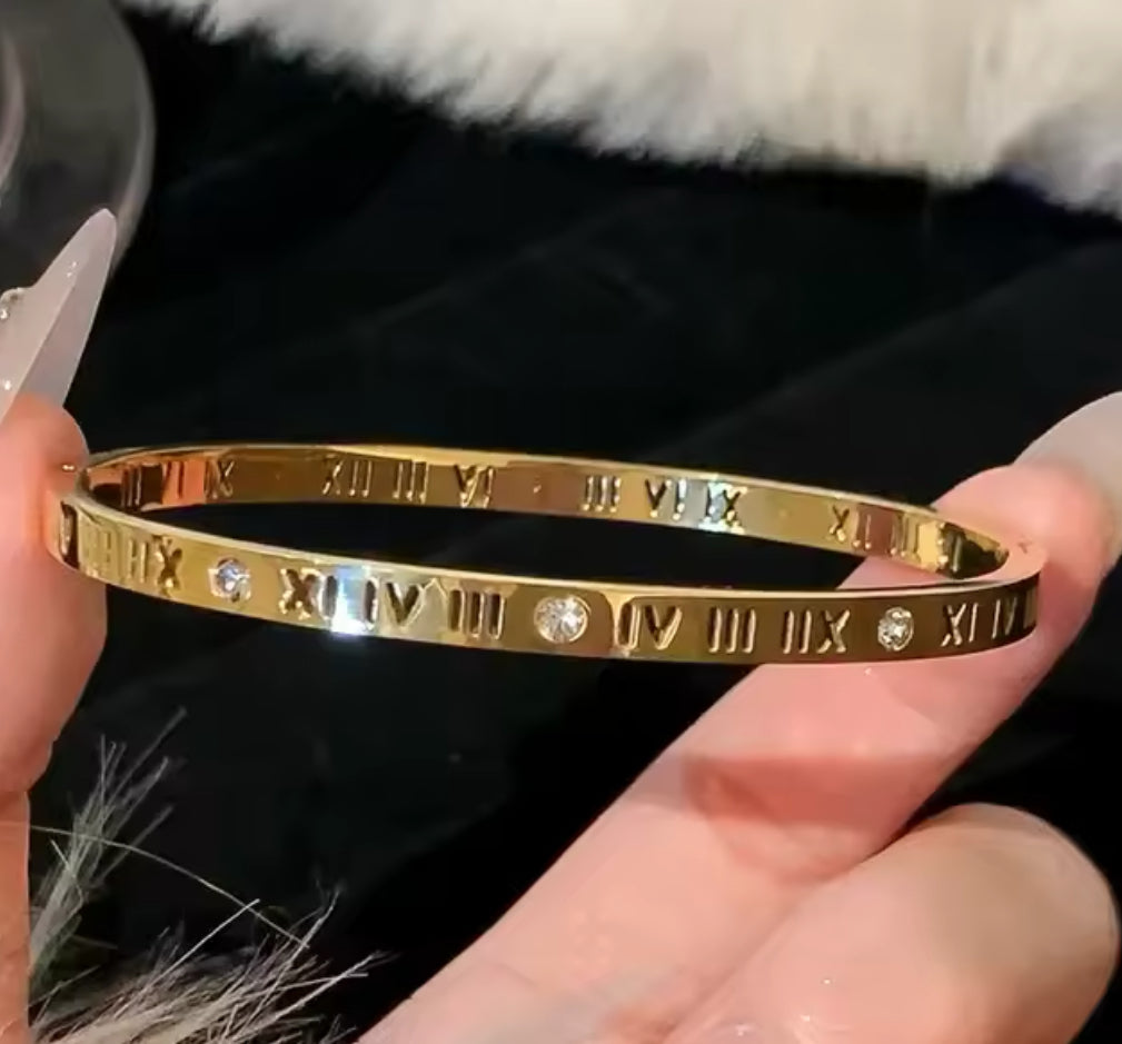 Close up side view of elegant 18k Gold plated stainless steel, Cartier dupe, designer inspired, roman numeral bangle bracelet with a smooth, polished finish and inlayed crystals, designed with a lightweight and tarnish resistant material for timeless sophistication.