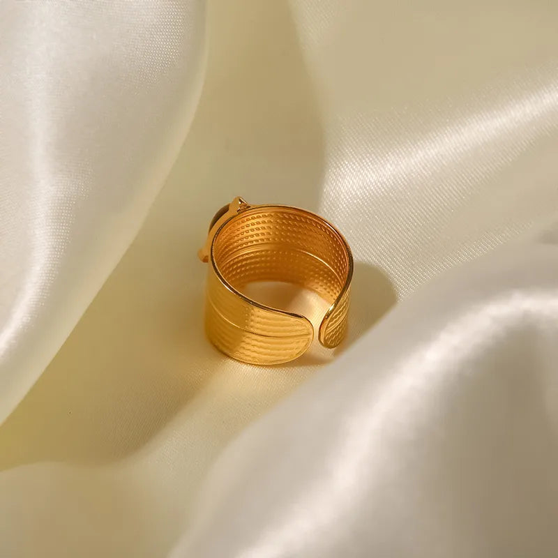 Front view of bold statement ring that features a striking tiger's eye center stone set in a luxurious gold-plated, tarnish resistant, long lasting stainless steel band. The thick adjustable band adds a touch of drama, making it the perfect accessory for those who dare to stand out.